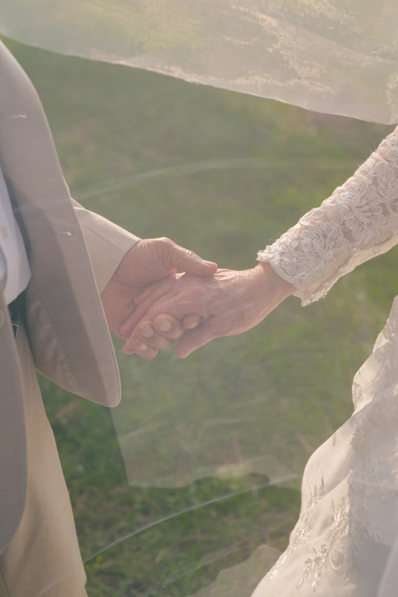 Close-up of couple holding hands under a veil